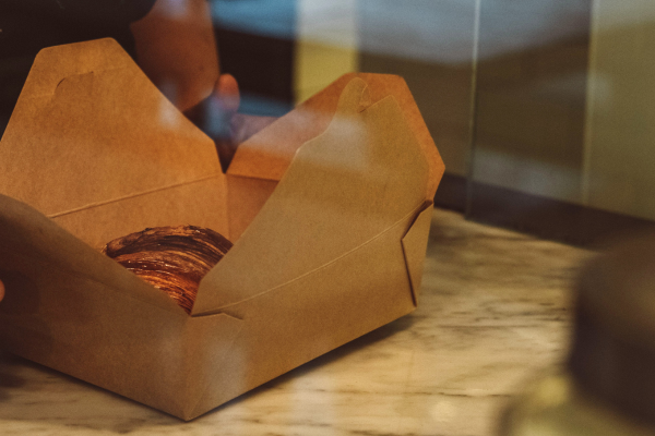 Someone packaging leftover pastries into a kraft takeaway box for a Too Good To Go collection, helping to reduce food waste in a bakery.