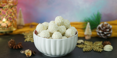 White coconut and mango truffles coated in desiccated coconut and presented in a bowl with festive decorations.