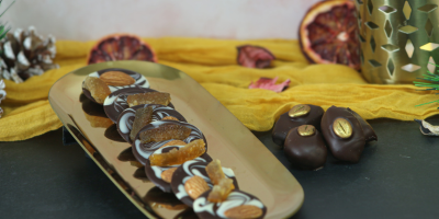 Dark chocolate with white chocolate swirls, topped with orange, almonds and nuts, arranged on a gold tray.