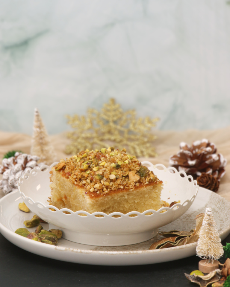 Baklava-inspired orange, honey and pistachio cake topped with chopped pistachios, styled with festive decorations.