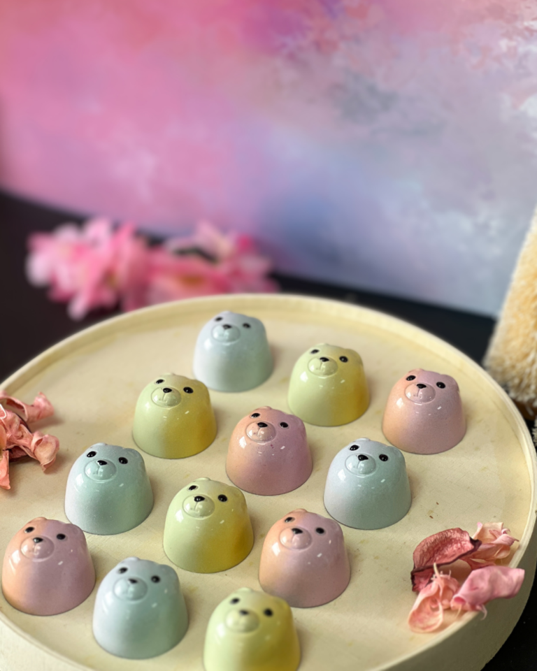 Pastel-coloured Miso Caramel Crunch Bear chocolates arranged on a round tray with pink flowers.